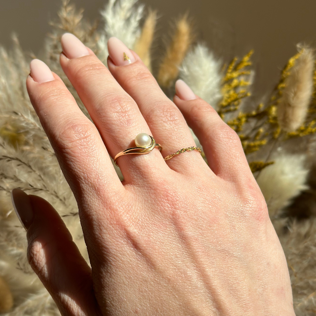 Hand wearing a gold ring with a pearl on a permanent jewelry ring