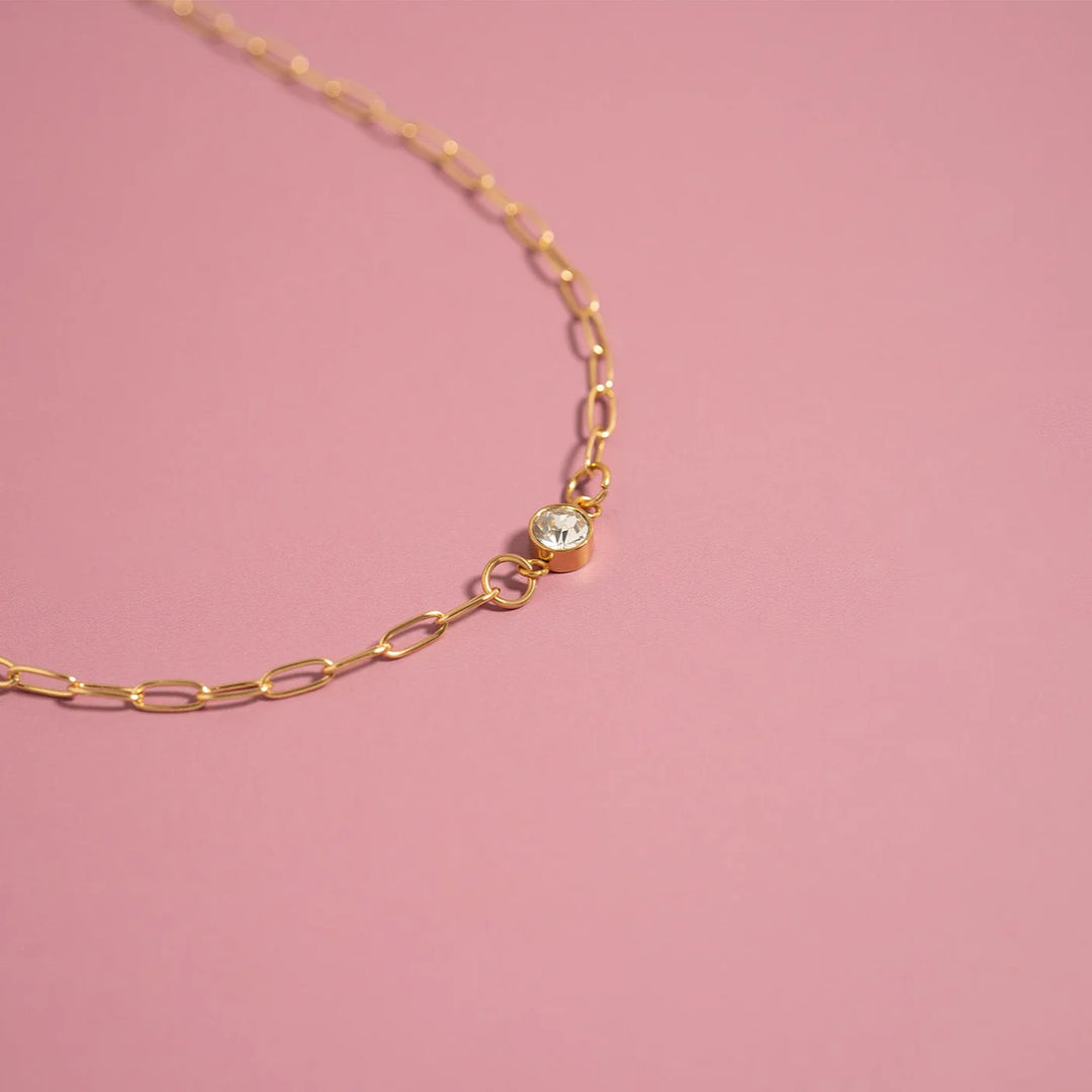 Gold chain necklace with a small green gemstone on a pink background