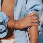 Person wearing a light blue shirt with colorful permanent jewelry bracelet stack