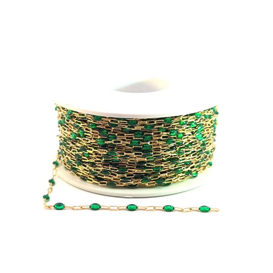 Spool of gold chain with green beads on a white background