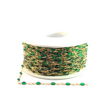 Spool of gold chain with green beads on a white background