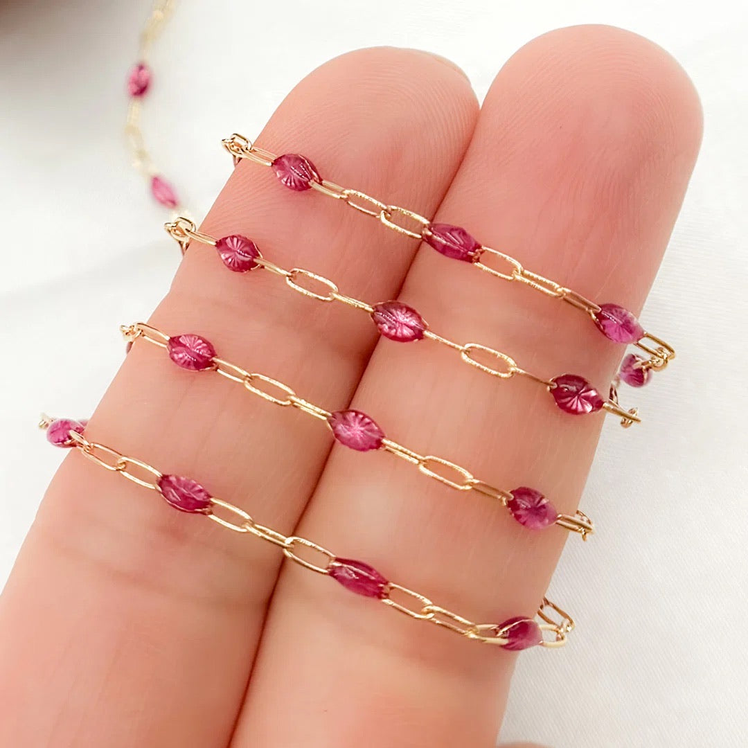 Gold chain with pink beads on a hand against a white background
