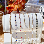 Set of beaded necklaces on a white cylindrical stand with a blurred floral background