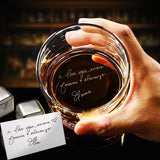Hand holding a glass of whiskey with a personalized message, set against a blurred bar background.