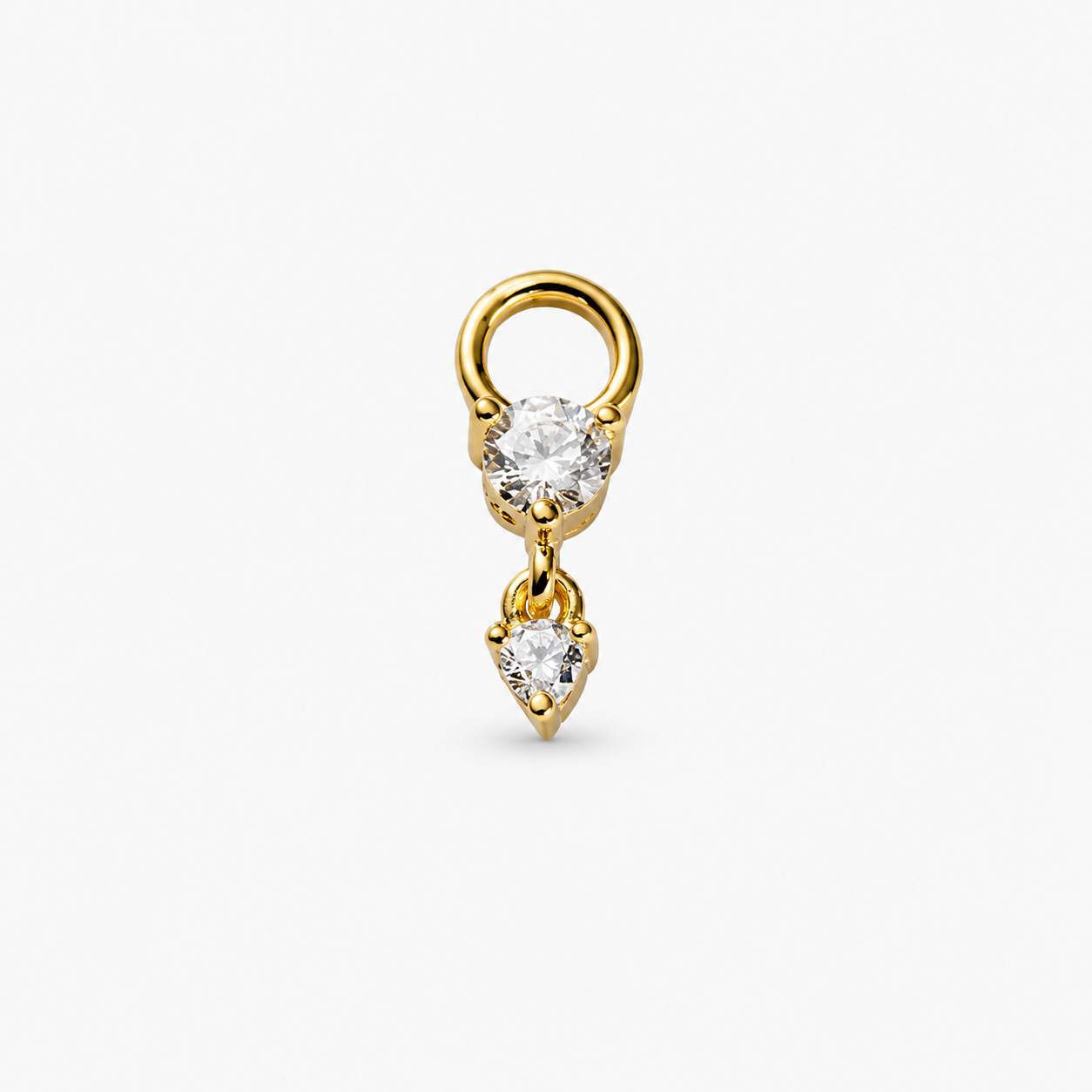A gold ring earring featuring a round clear gemstone and a dangling heart-shaped clear gemstone, set against a plain light gray background.