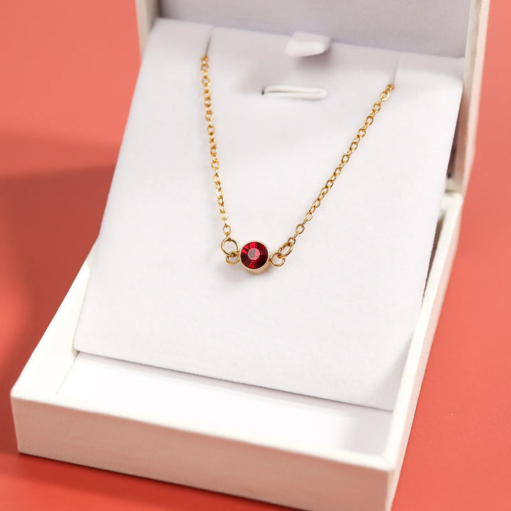 Gold necklace with a red gemstone in an open white box on a pink background