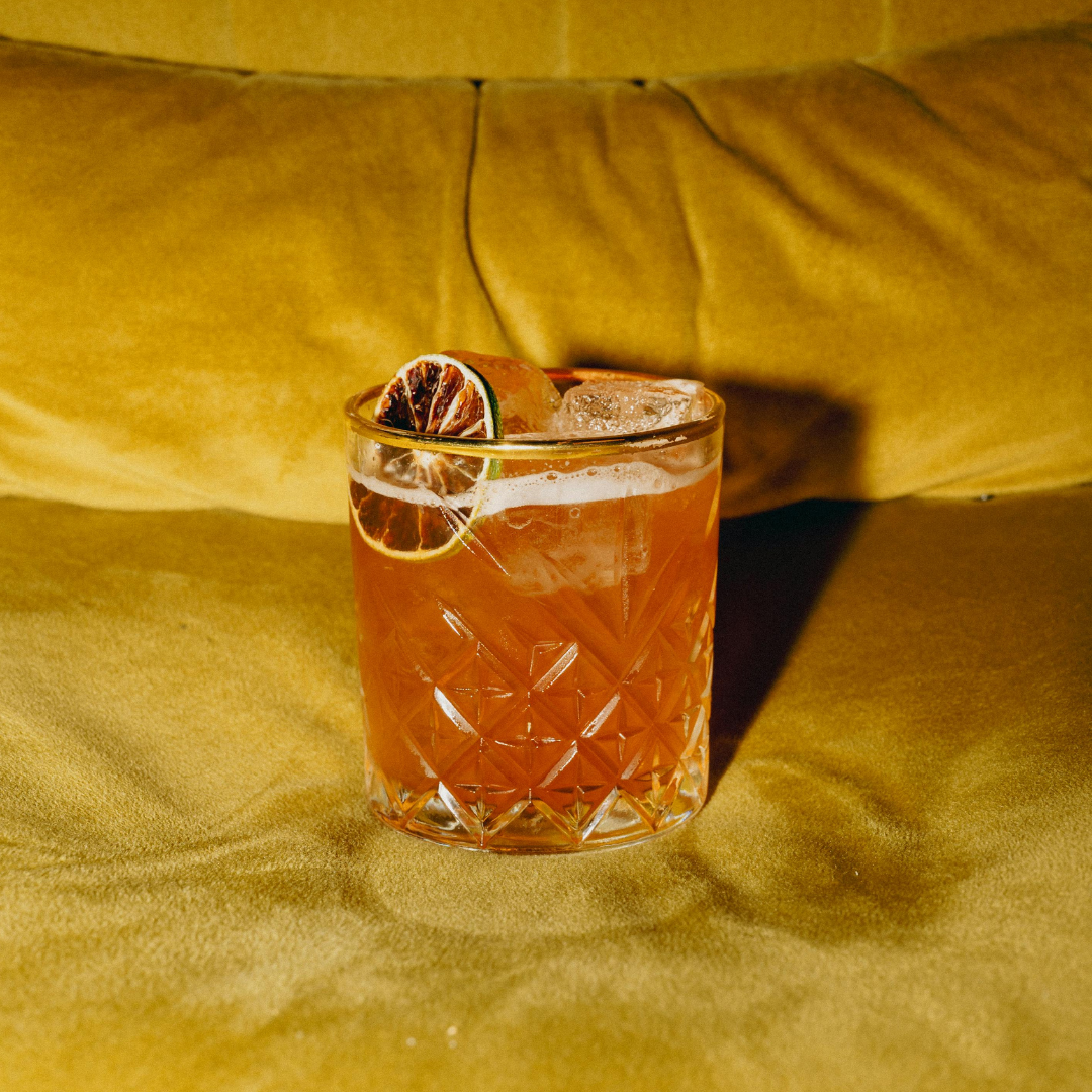 Glass of orange cocktail with a slice of orange on a yellow fabric background