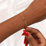 Gold bracelet with a January red garnet gemstone on a wrist against a white background
