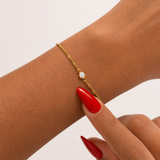 Gold bracelet with a opal charm on a wrist with red nail polish against a light background