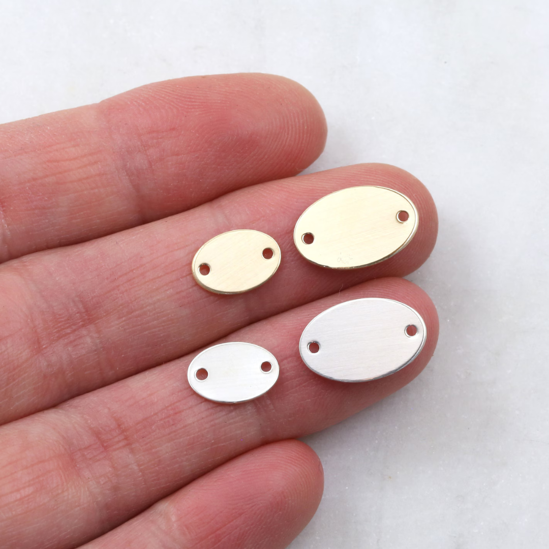 Gold and silver oval-shaped pendants on a person's hand against a white background