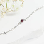 Silver bracelet with a red gemstone on a white background with flowers