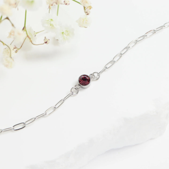 Silver bracelet with a red gemstone on a white background with flowers