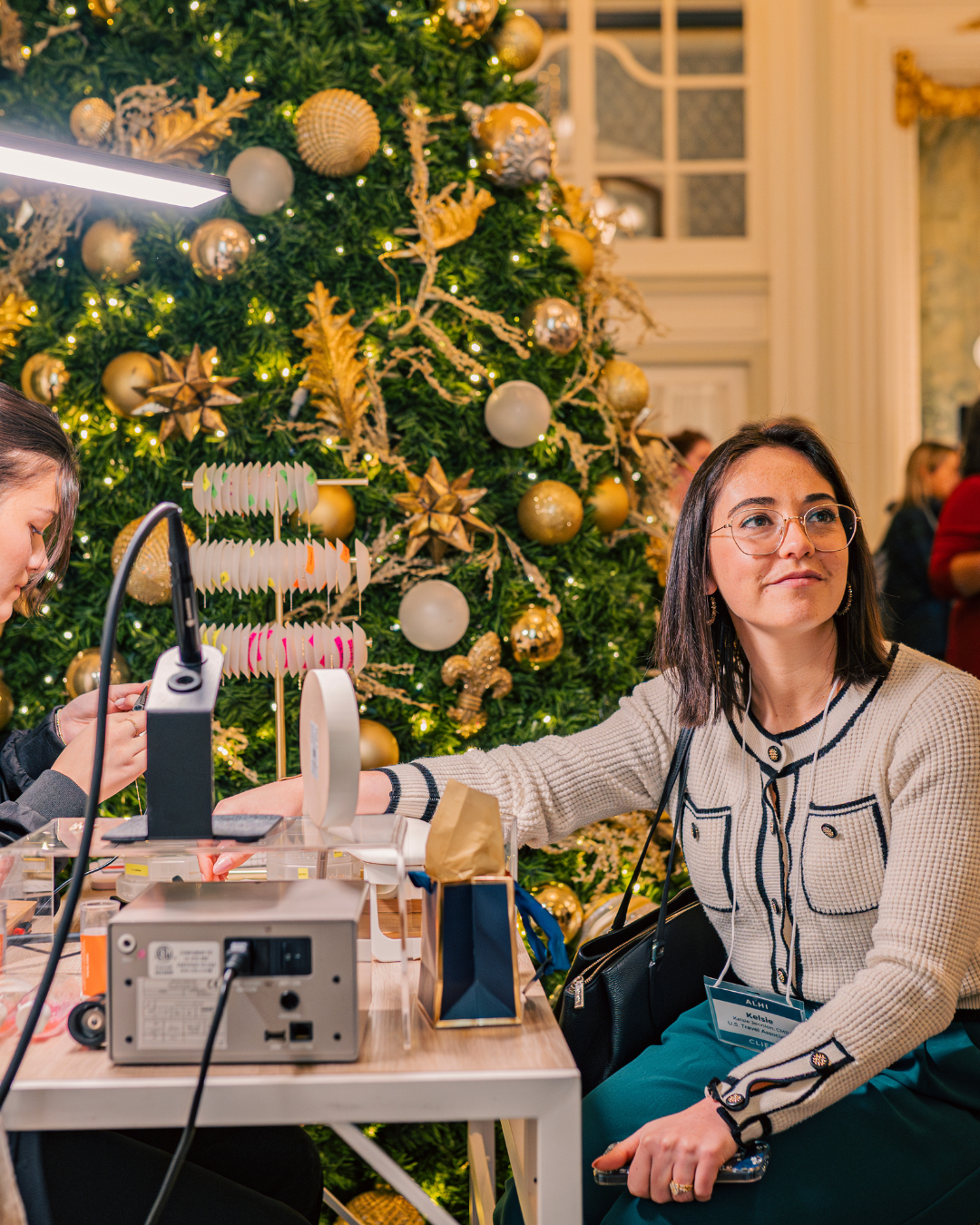 Woman getting permanent jewelry welded in front of a Christmas Tree.