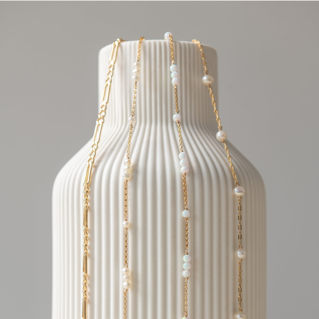 Gold chain and pearl necklace on a textured white vase against a gray background