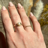 Permanent Jewelry Store - Hand wearing a gold ring with a pearl on a blurred natural background