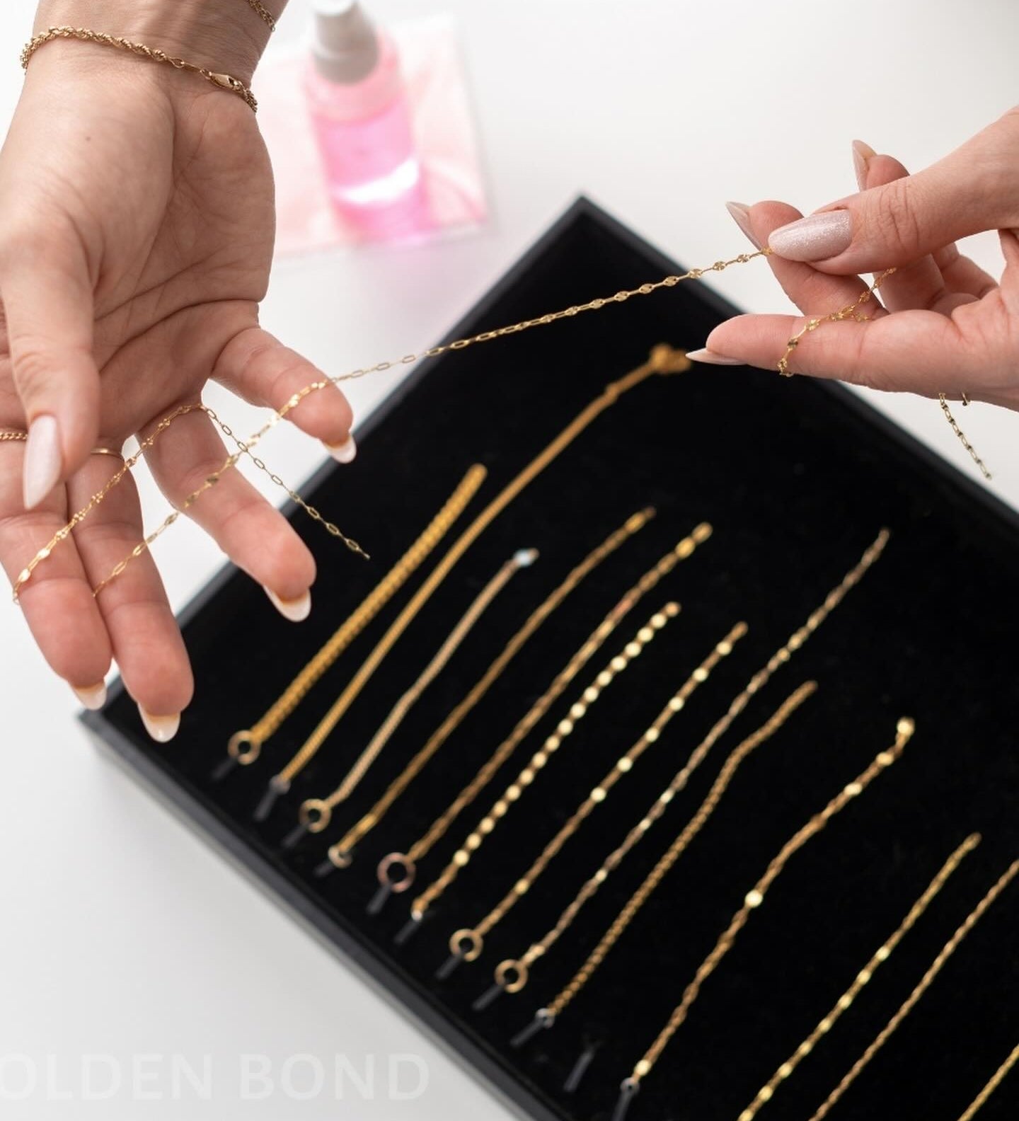 Gold chains for permanent jewelry training displayed in a black tray with hands holding one necklace.