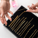 Gold chains for permanent jewelry training displayed in a black tray with hands holding one necklace.