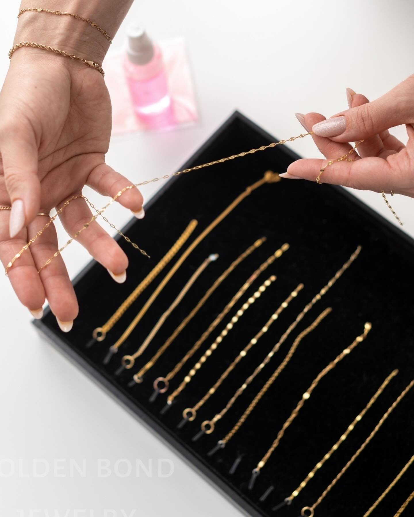 Gold chains for permanent jewelry training displayed in a black tray with hands holding one necklace.