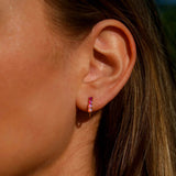 Close-up of an ear wearing a small hoop earring with pink gemstones.