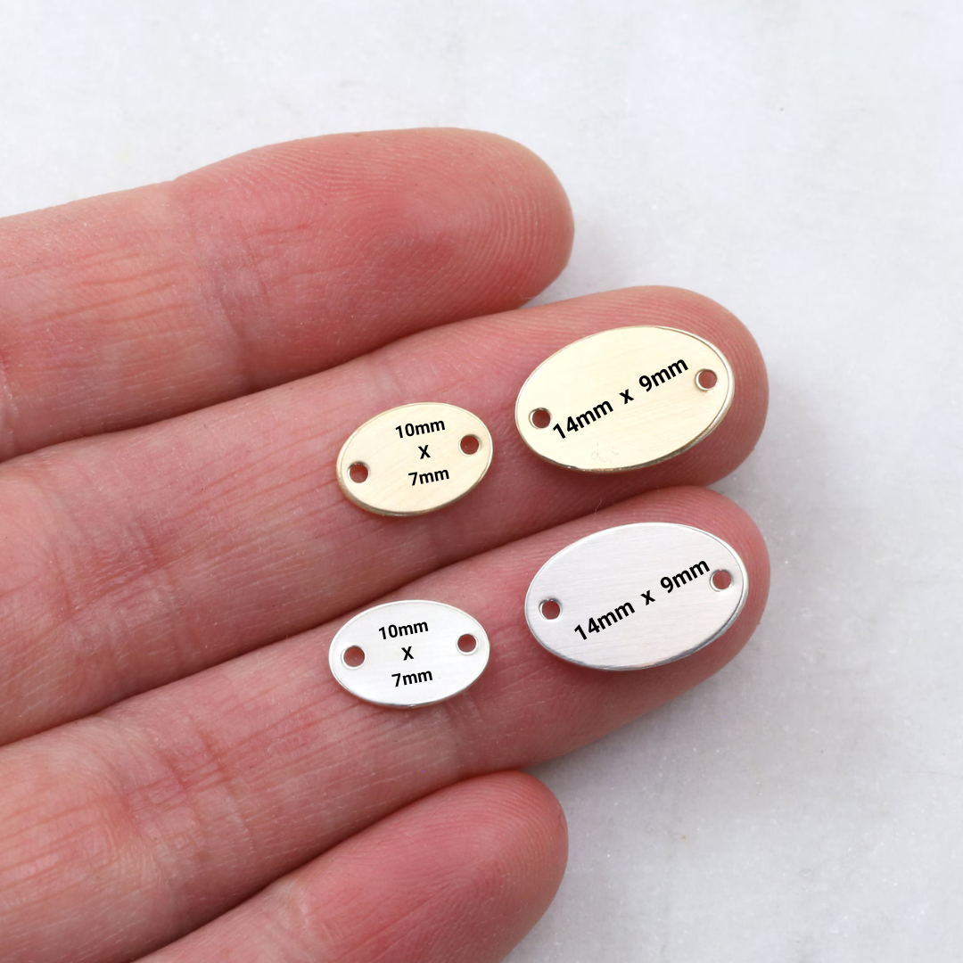 Gold and silver oval metal tags with measurements held between fingers on a white background