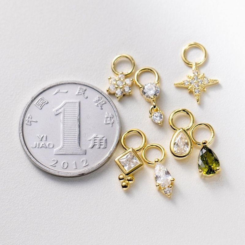 Gold jewelry charms with embedded stones next to a Chinese coin on a light gray background