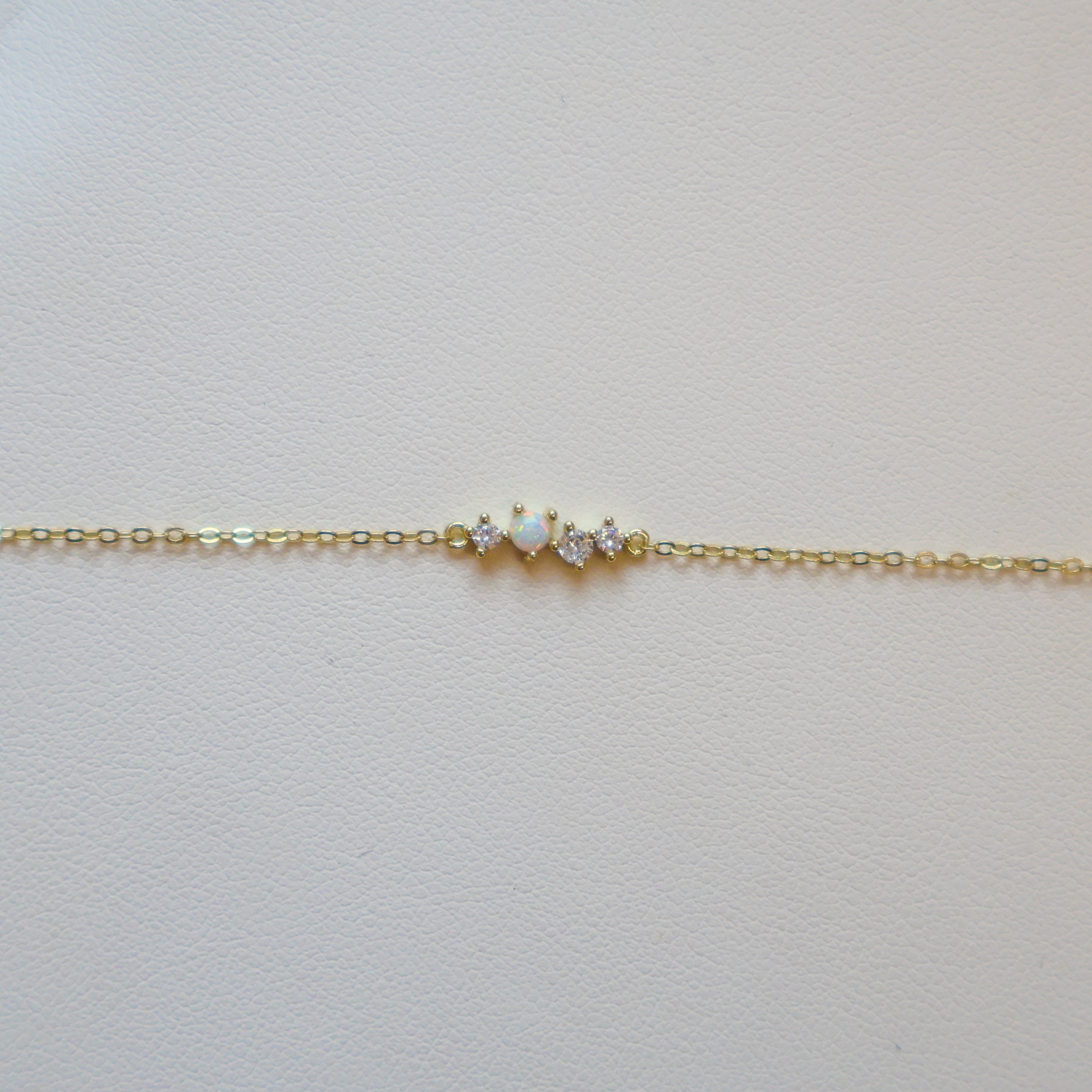 Gold bracelet with one opal and three small diamonds on a white leather surface