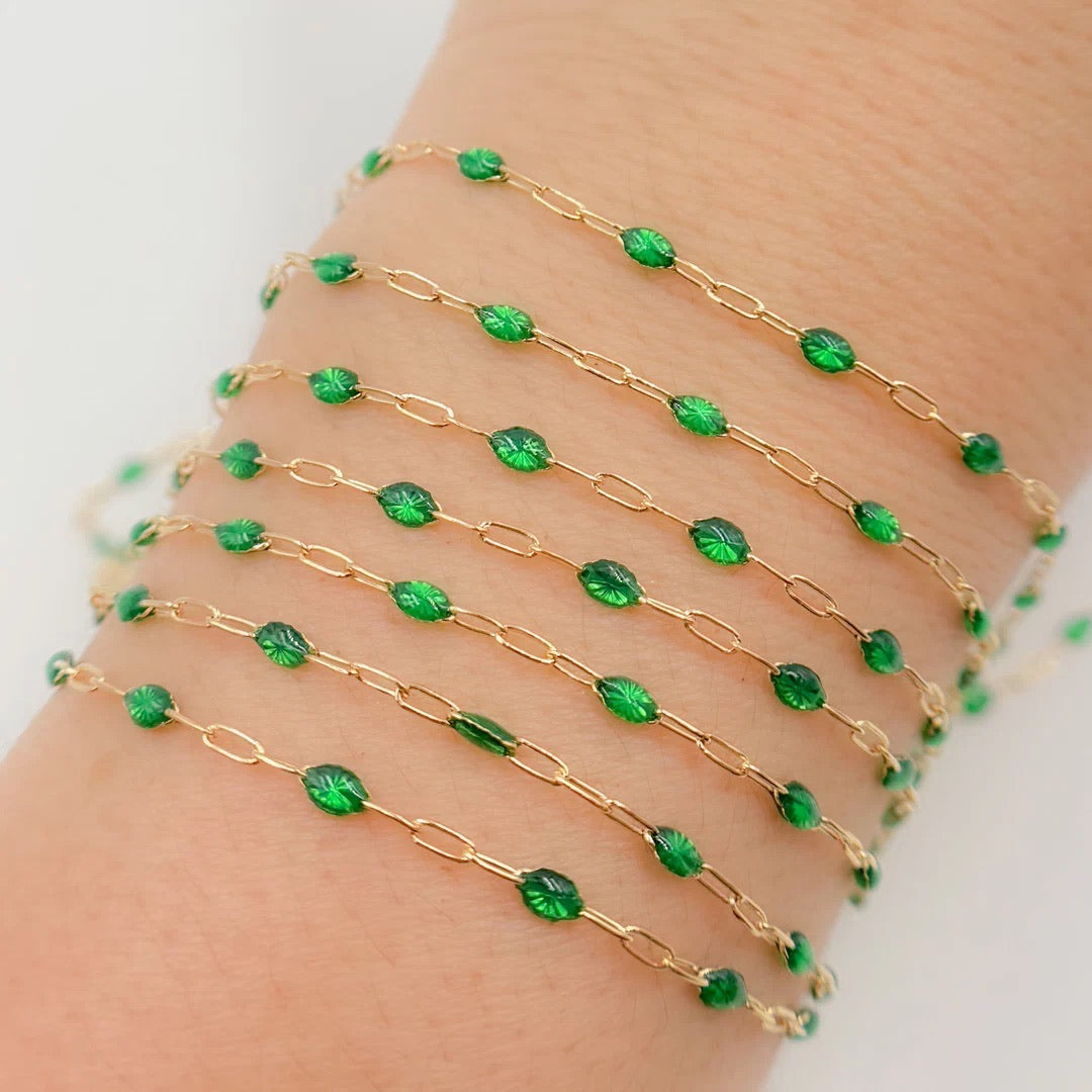 Gold chain bracelet with green beads on a wrist against a white background