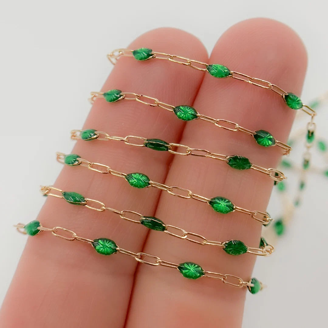 Gold chain with green beads held on a hand against a white background