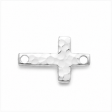 A silver cross-shaped jewelry charm with a hammered texture and two circular holes, shown on a plain white background.